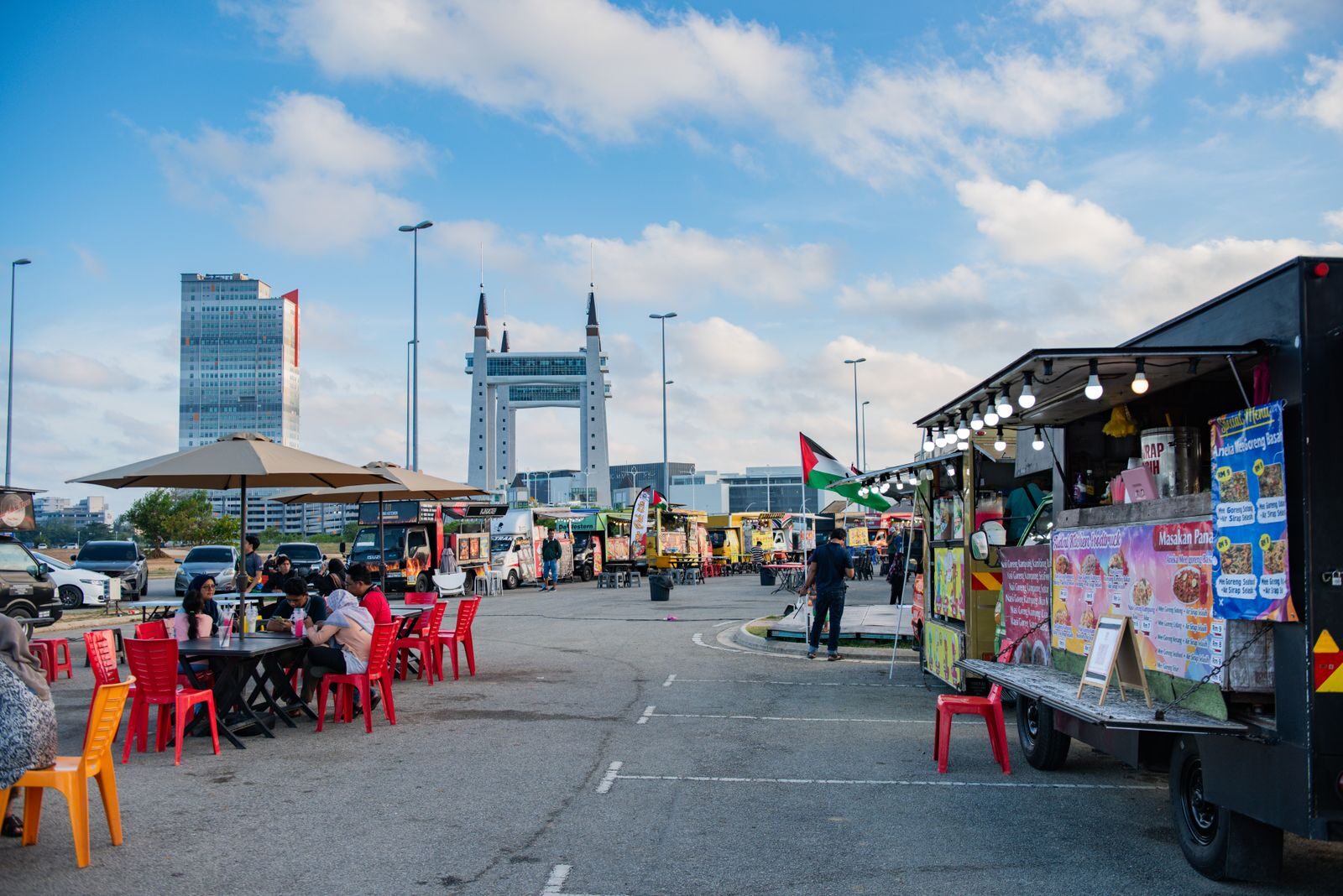 Lively outdoor food truck scene at KTCC, Kuala Terengganu, with people enjoying meals under a bright sky.