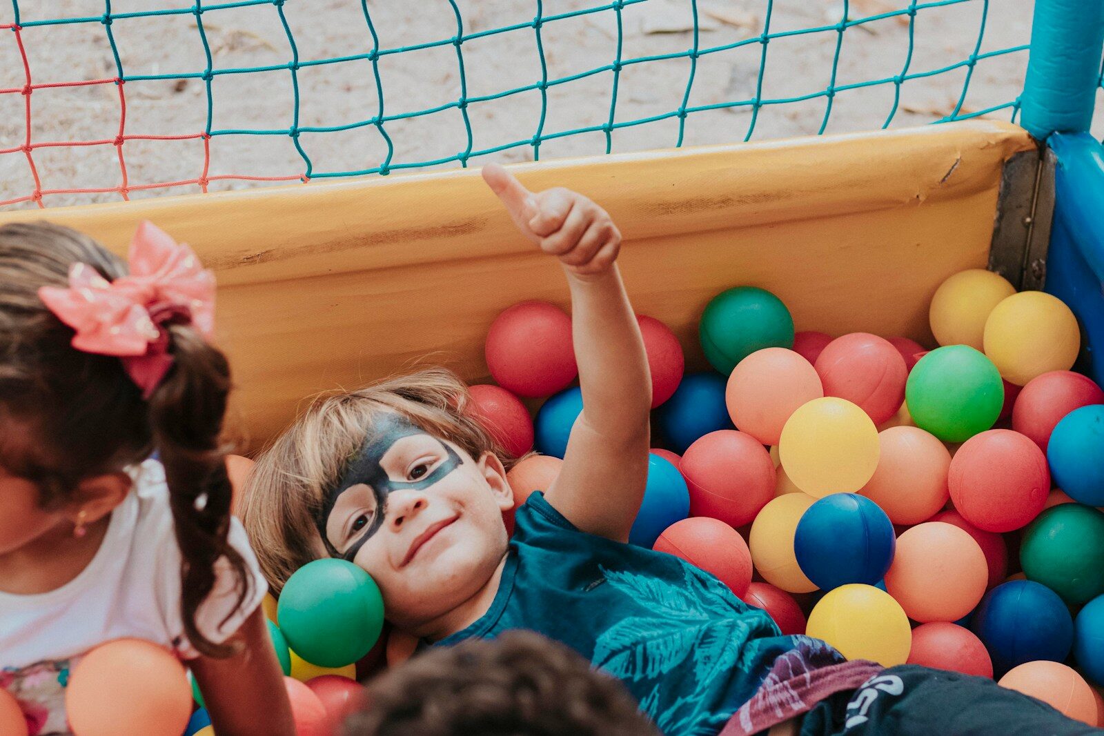 A child with face paint giving a thumbs up in a colorful ball pit